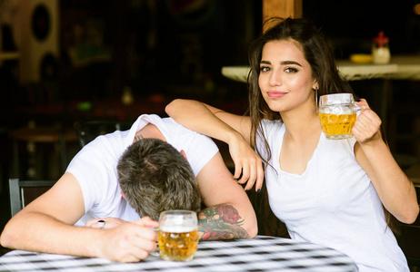 情侣恋爱约会喝啤酒.醉酒的人在餐桌上睡着了, 女孩喝满了啤酒杯.